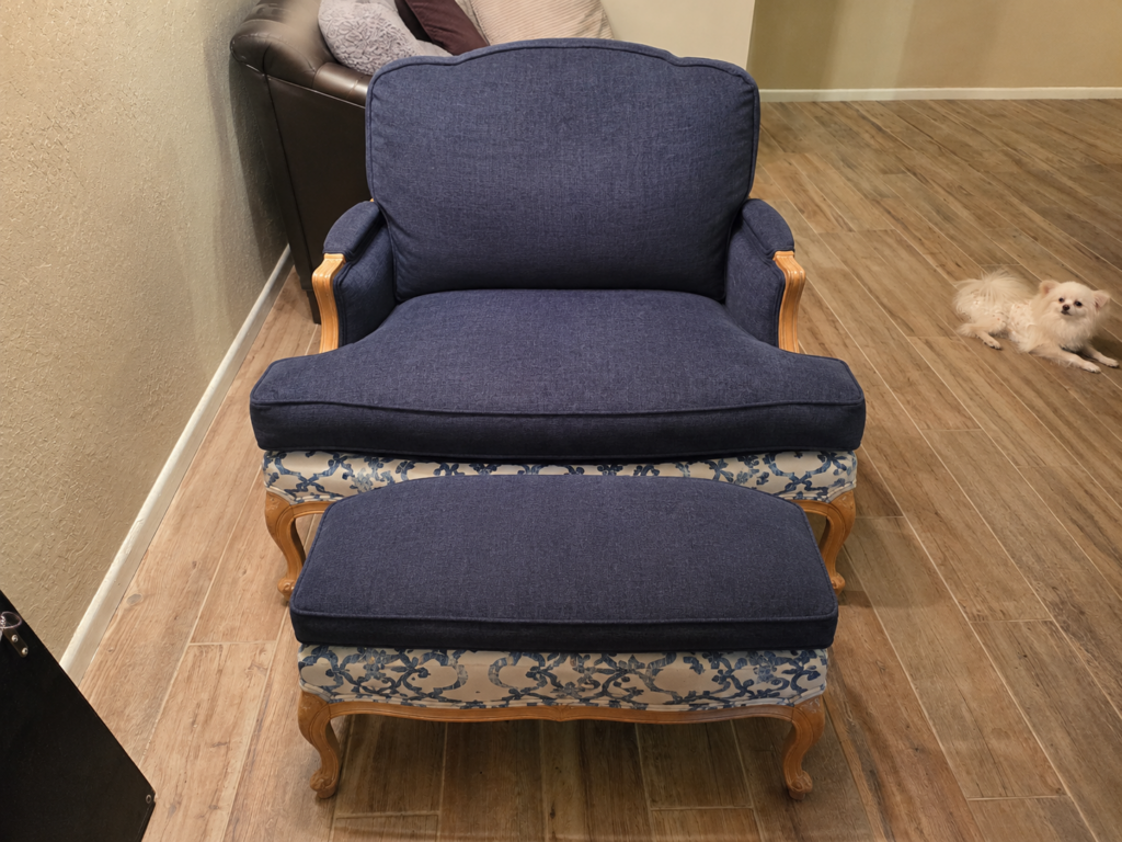 Reupholstered vintage French Bergère armchair and matching ottoman with deep navy blue cushions and a cream and blue damask pattern on the lower base frames.